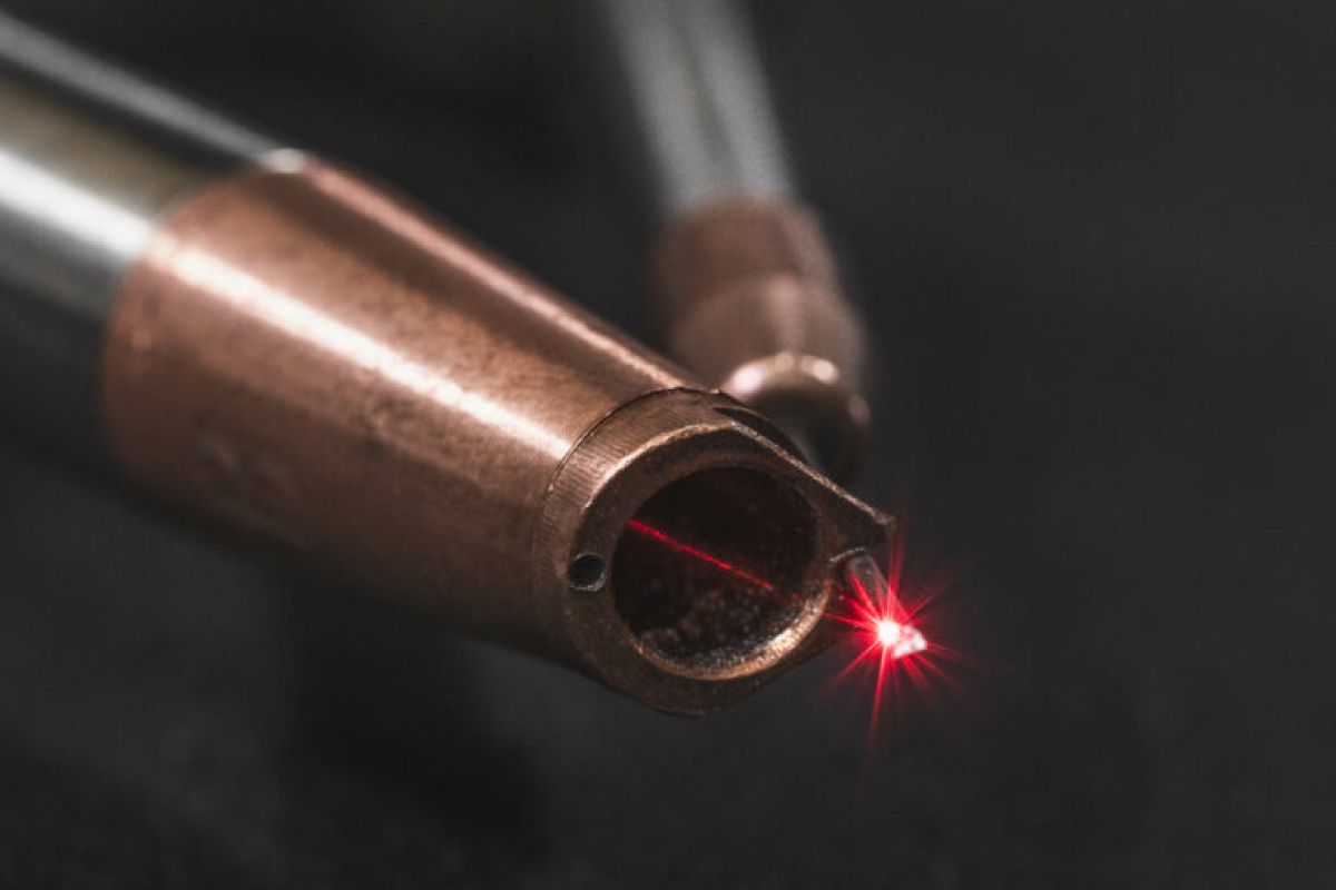 Närbild av ett metallobjekt som avger en röd laserstråle från dess spets, mot en mörk bakgrund.