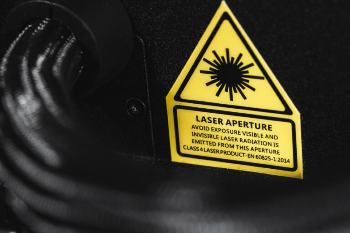 Närbild av en varningsetikett på en enhet som anger, "LASERBLIPPARE. Undvik exponering, synlig och osynlig laserstrålning sänds ut från denna bländare. Klass 4 laserprodukt. EN 60825-1:2014.